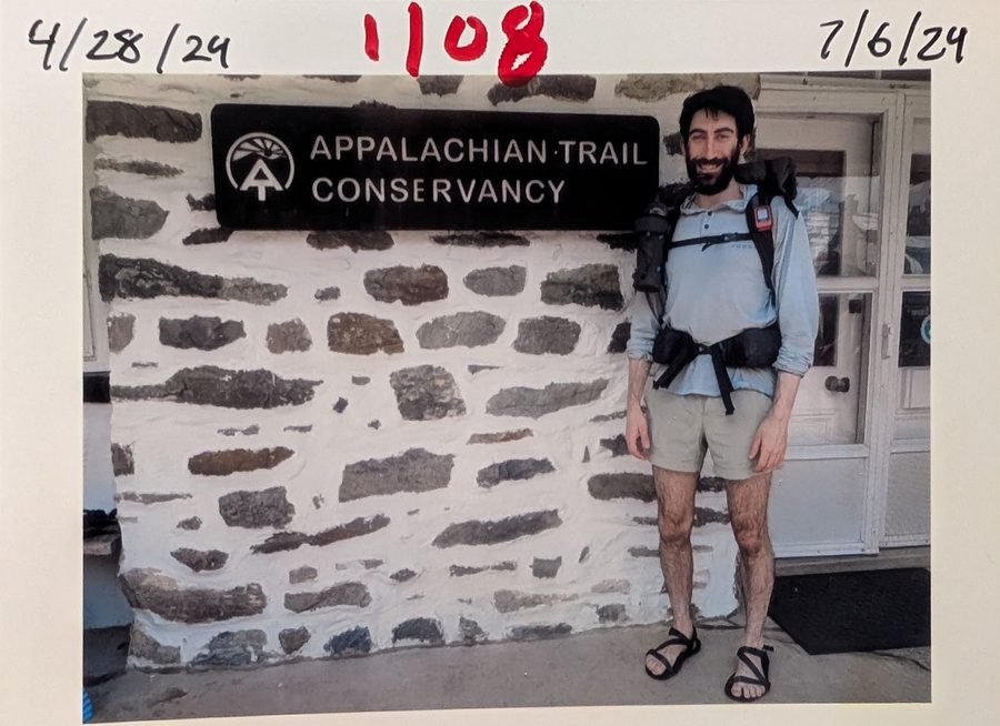 A photo print of Brennon in hiking clothes and sandals, pack on, smiling beside the Appalachian Trail Conservancy sign on a stone building. Handwritten across the top: 4/28/24, 1108 in red, and 7/6/24.