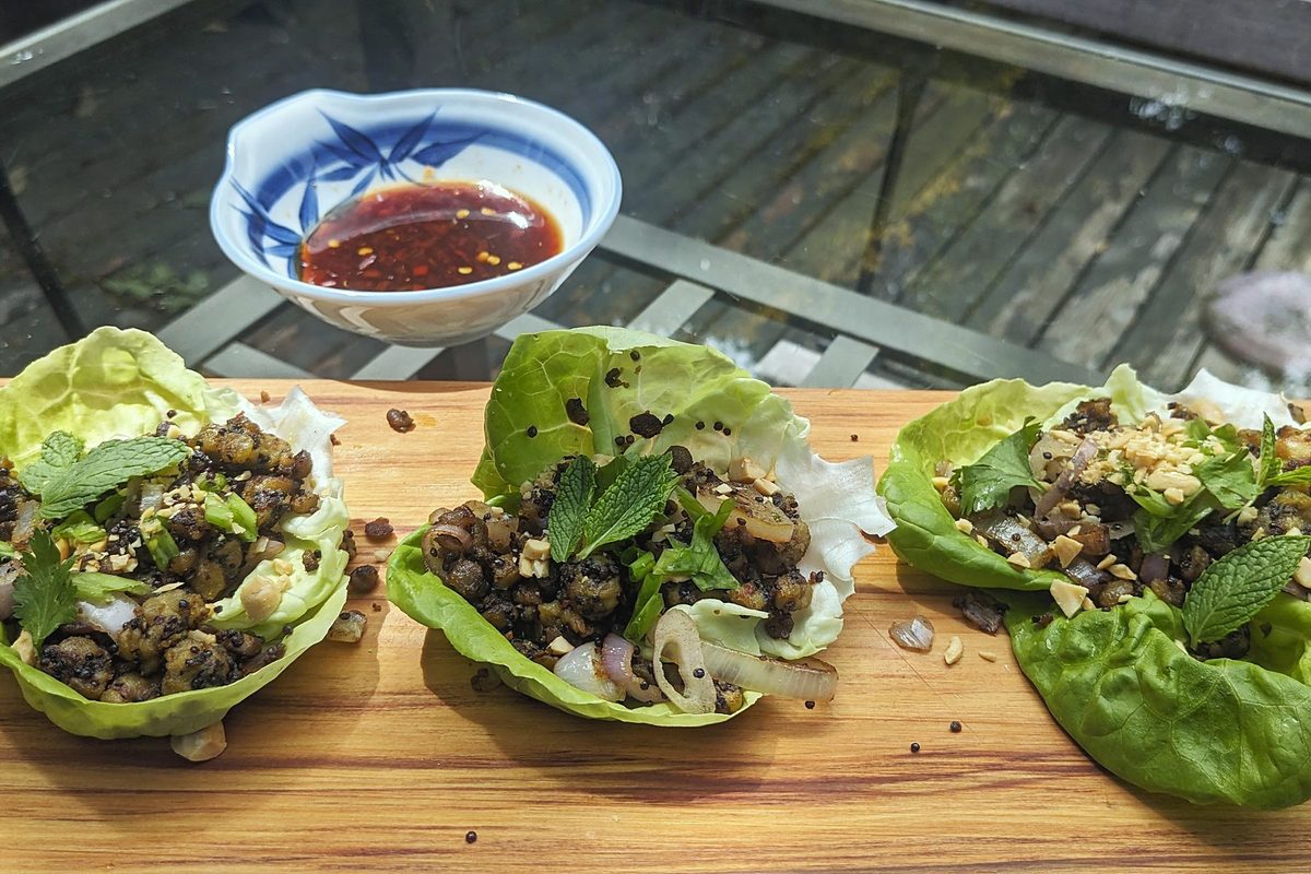 Three butter lettuce cups filled with tempeh crumbles, shallot, mint and peanuts, with a bowl of chili-vinegar dipping sauce
