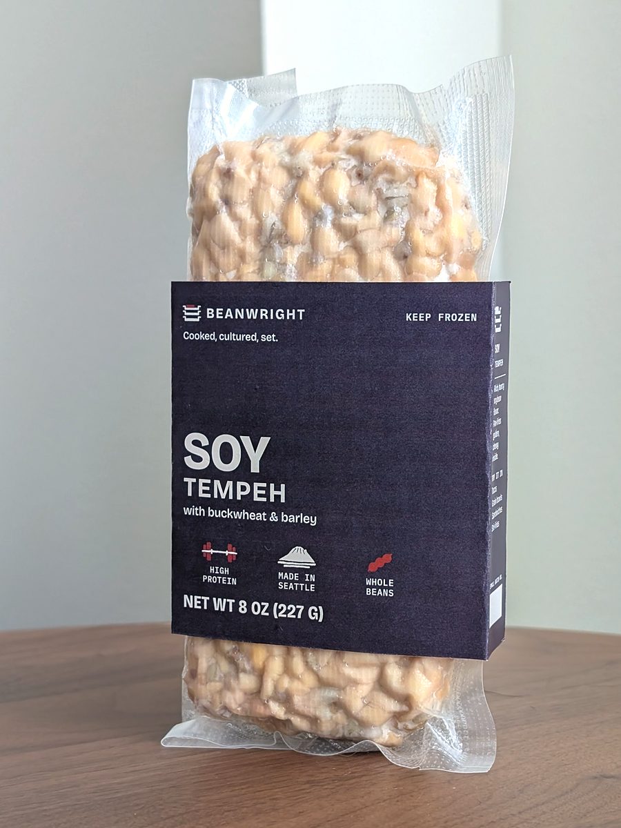 Soy tempeh in its slate band. Pale soybeans show through the vacuum pack above and below.