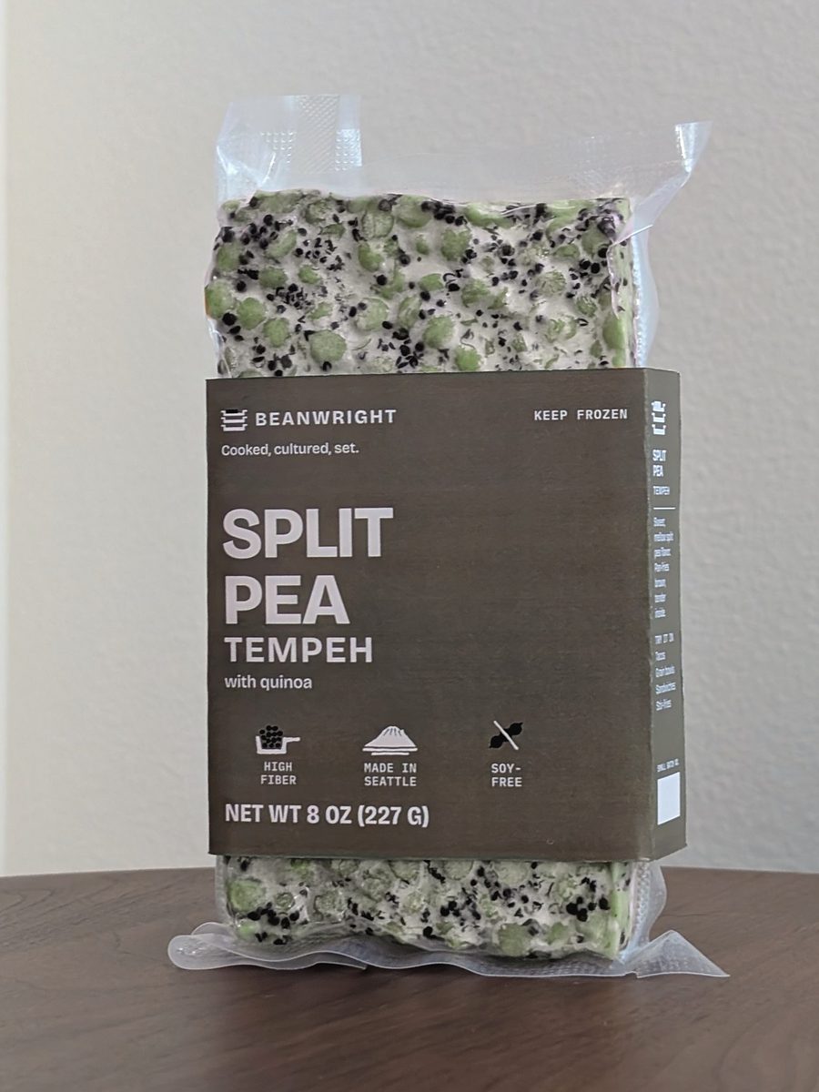 Split pea tempeh in its olive band. Green split peas and dark quinoa show through the vacuum pack above and below.